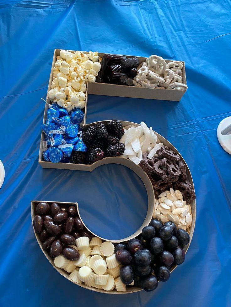 the letter c is made out of grapes, nuts and chocolates on a blue table cloth