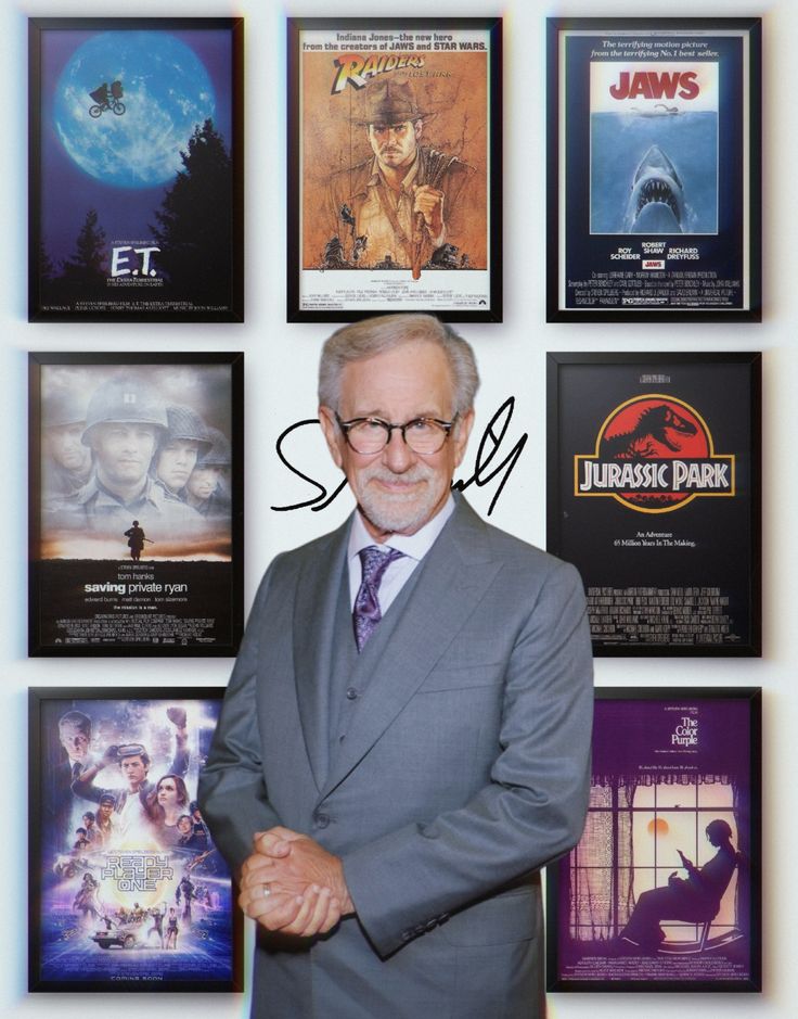 an older man in a suit and tie standing next to movie posters on the wall