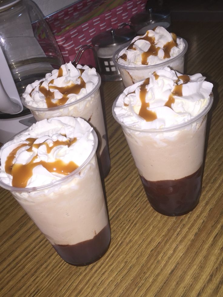 three drinks with whipped cream and caramel drizzled on them sitting on a table