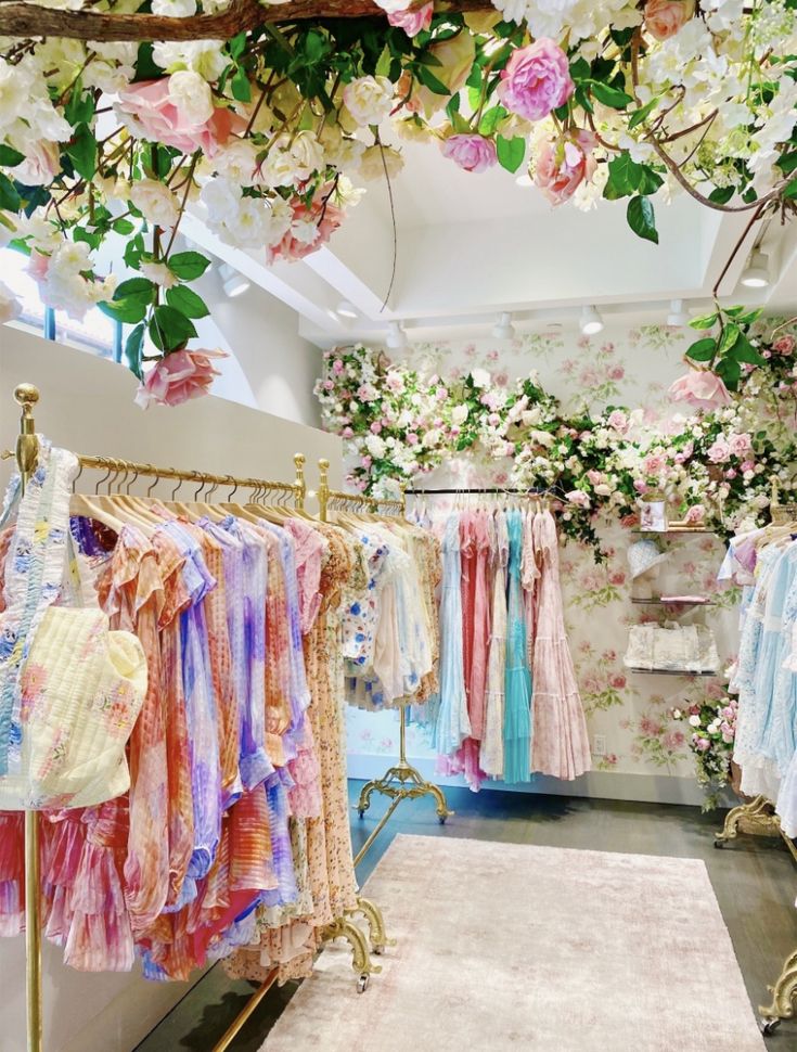 a clothing store filled with lots of clothes and flowers hanging from the ceiling above it