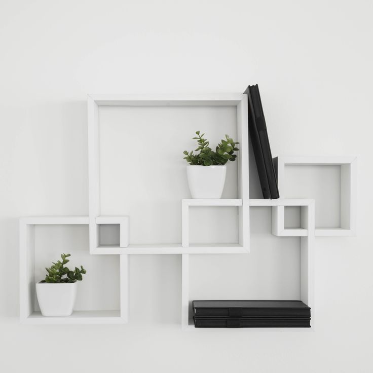 three white shelves with plants and books on them, one has a black book in the middle