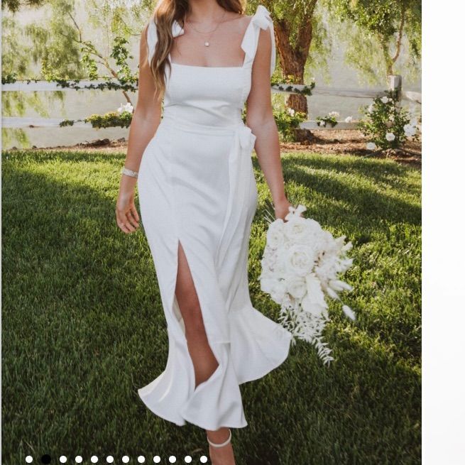 a woman in a white dress is holding a bouquet and posing for a photo on the grass