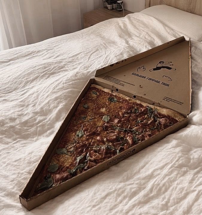 an open pizza box sitting on top of a bed next to a white comforter