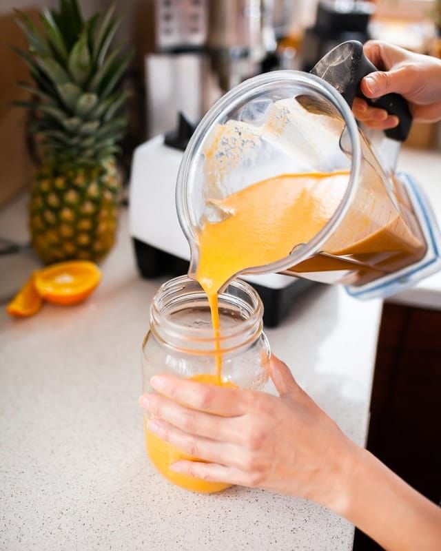 someone is pouring orange juice into a jar