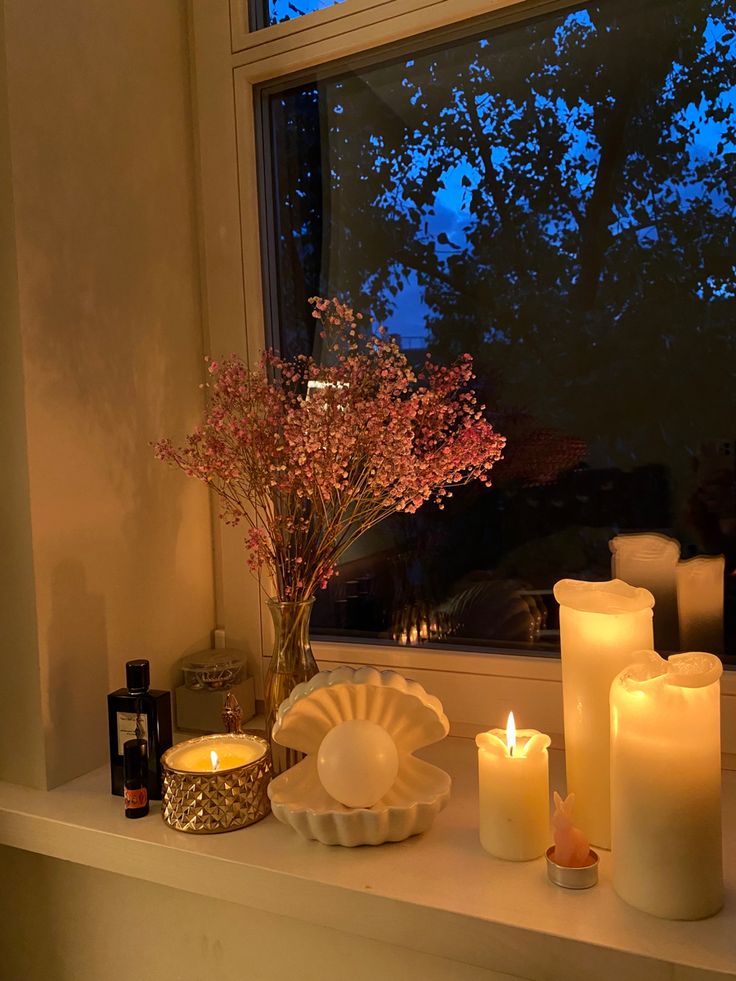 lit candles sit on a window sill next to a vase with flowers