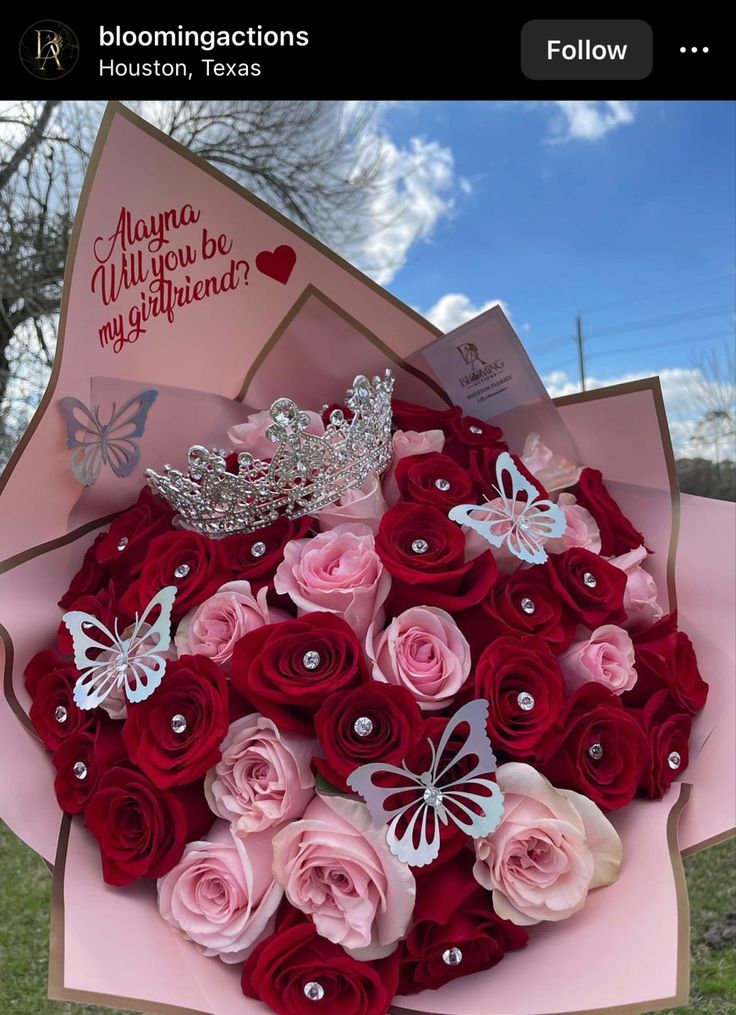 a bouquet of roses with a tiara on top in a pink paper flower box