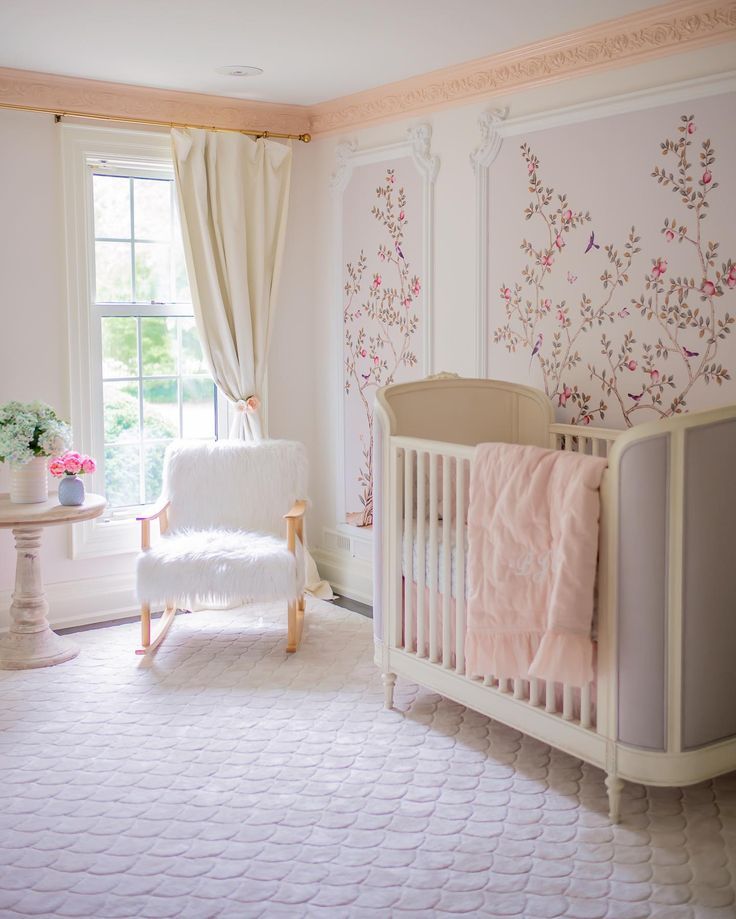 a baby's room with a white crib and pink flowers on the wall