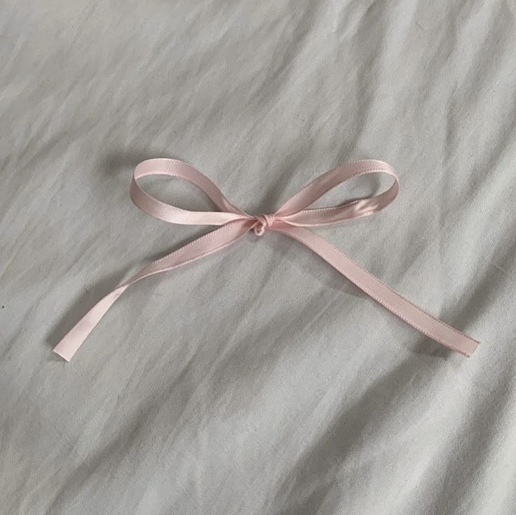 a pink ribbon tied on top of a white sheet with a knot around it's end