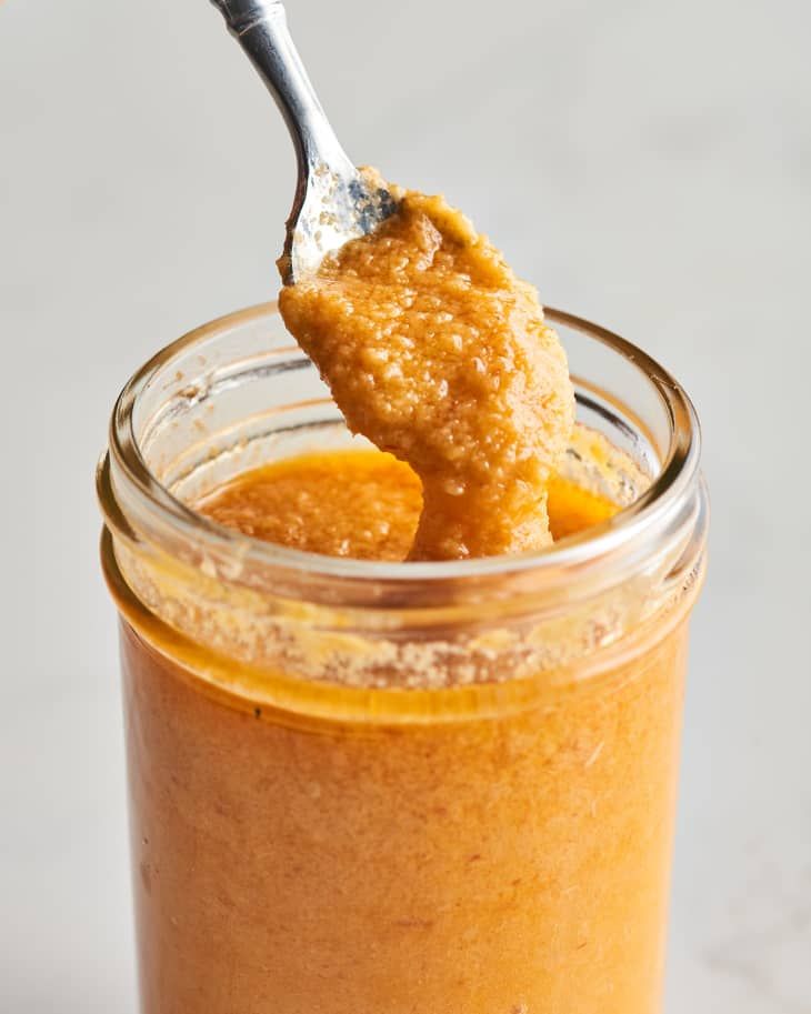 a spoon full of peanut butter on top of an orange sauce in a glass jar