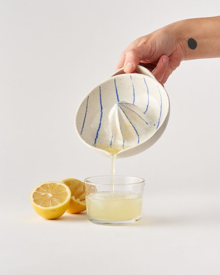 a person pouring orange juice into a glass with lemon wedges on the side and an orange slice next to it