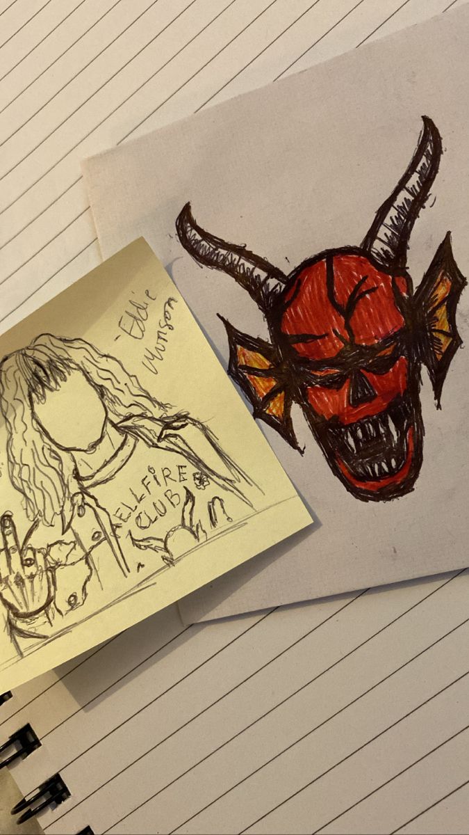 two notebooks with drawings on them next to a drawing of a demon's head