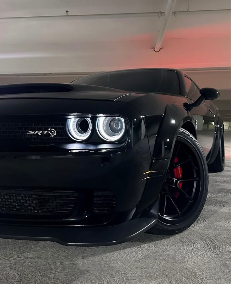 the front end of a black sports car in a parking garage with its lights on