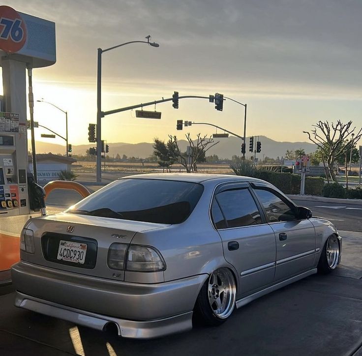 a silver car parked in front of a gas station at sunset with the sun going down