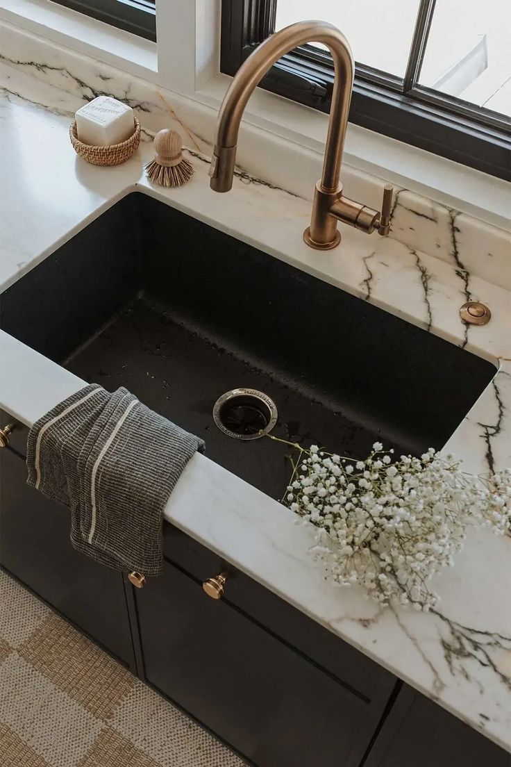 a kitchen sink with marble counter tops and gold faucets in front of a window