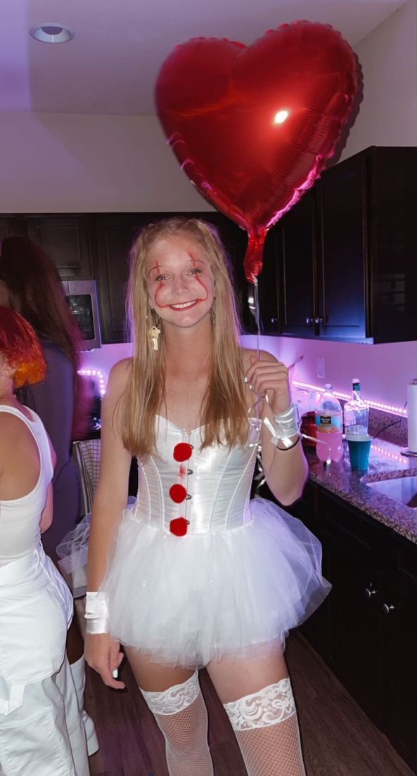 a girl in a white dress holding a red heart balloon