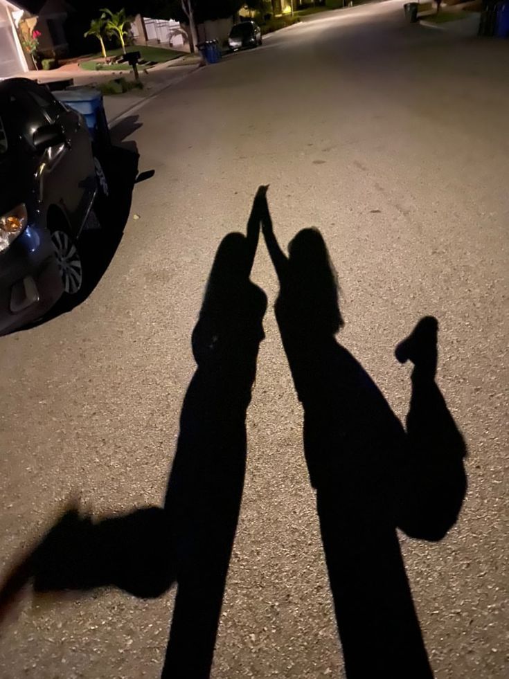 the shadow of two people holding hands in front of a parked car on a street at night