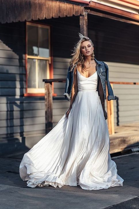 a woman in a white dress and jacket standing on the side of a road near a building