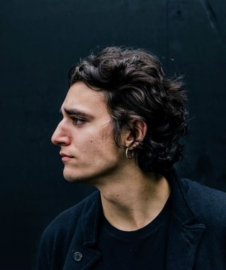 a young man with curly hair wearing a black jacket and looking off into the distance