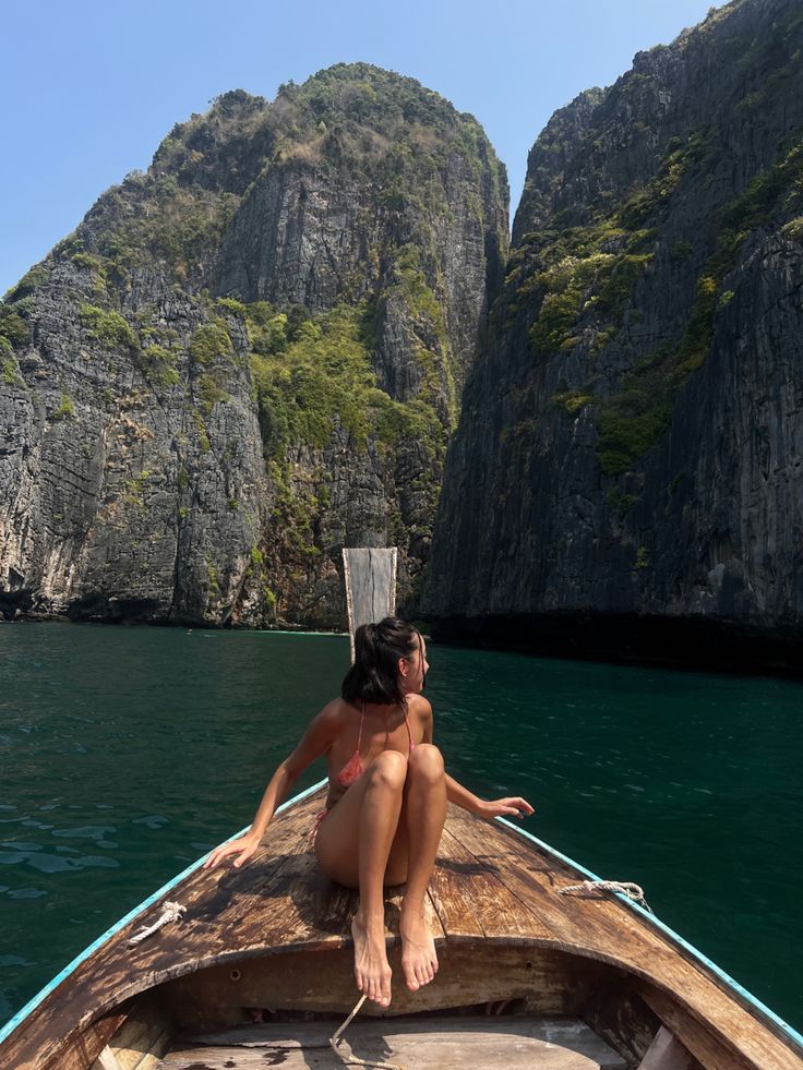 a woman sitting on the bow of a boat in front of some mountains and water