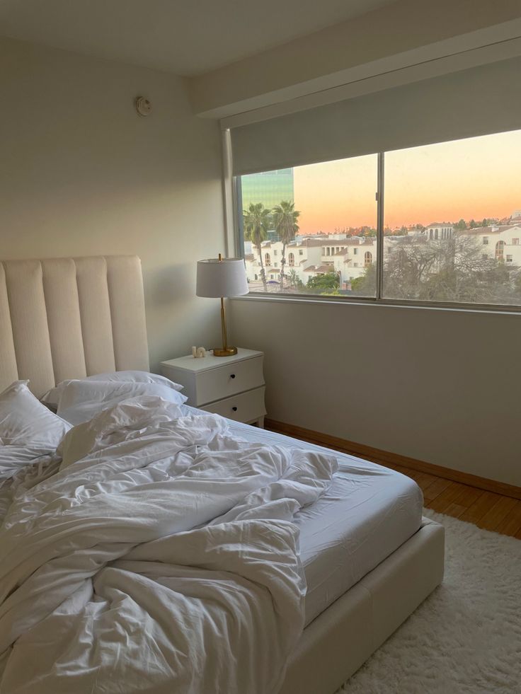 an unmade bed with white sheets and pillows in a bedroom next to a window