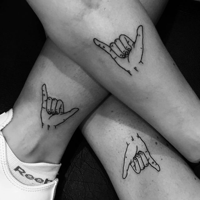 two people with matching tattoos on their legs, one holding the other's hand