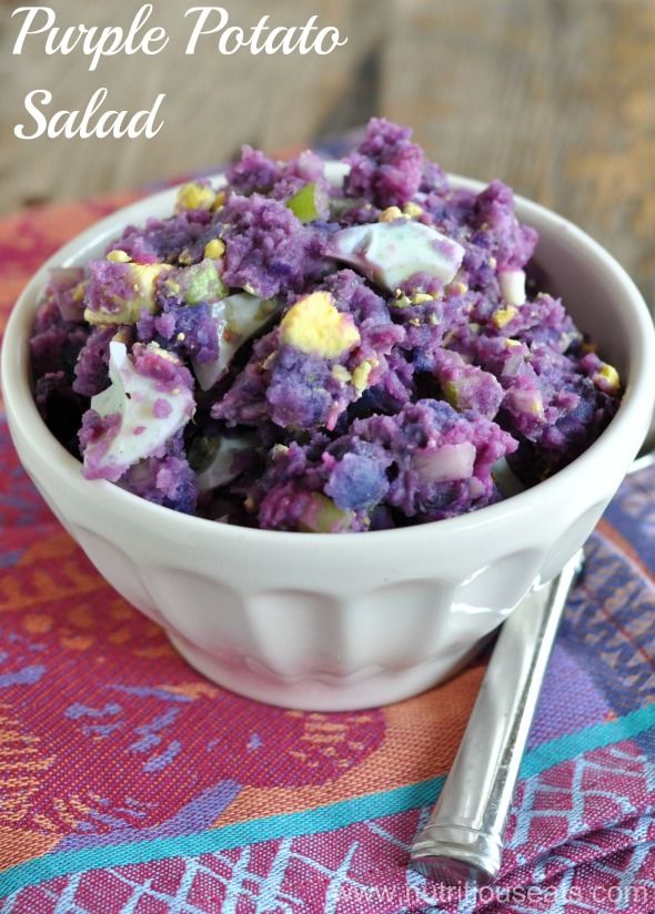 purple potato salad in a white bowl on a colorful table cloth with silverware next to it