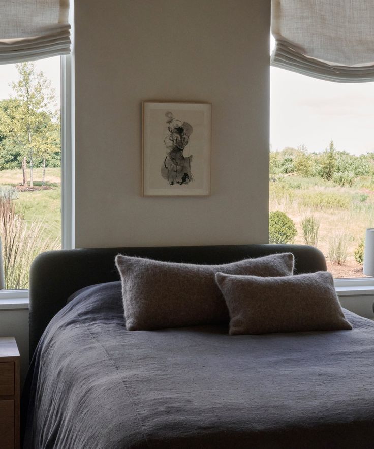 a bed with two pillows on top of it next to a window covered in curtains