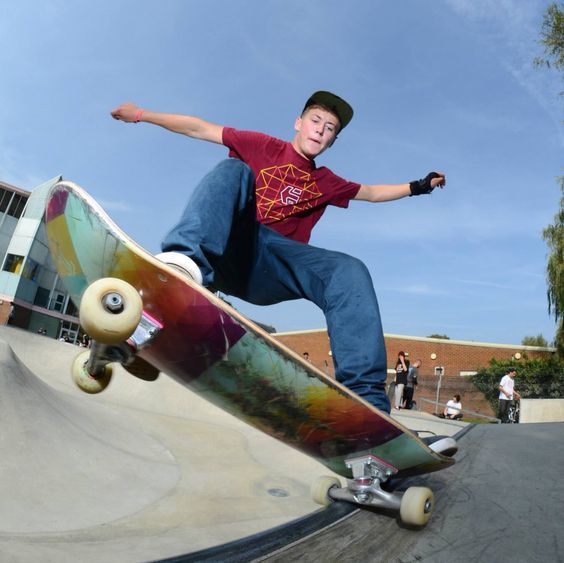 a young man riding a skateboard up the side of a cement ramp at a skate park