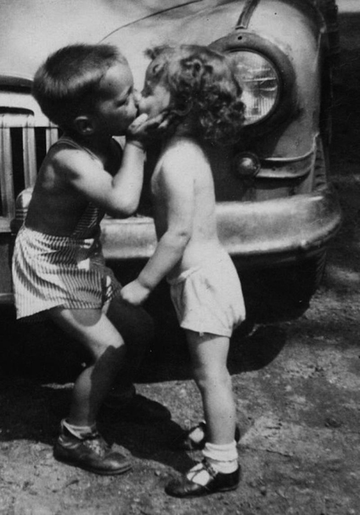 two young children standing next to an old car kissing each other's foreheads