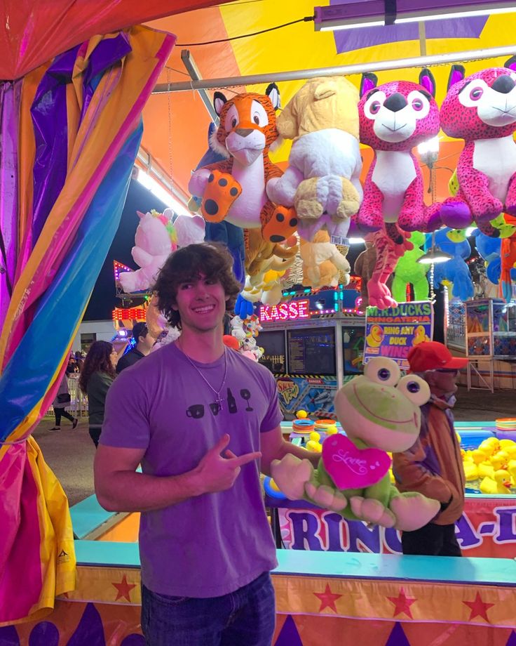 a man standing in front of a carnival booth with stuffed animals hanging from the ceiling