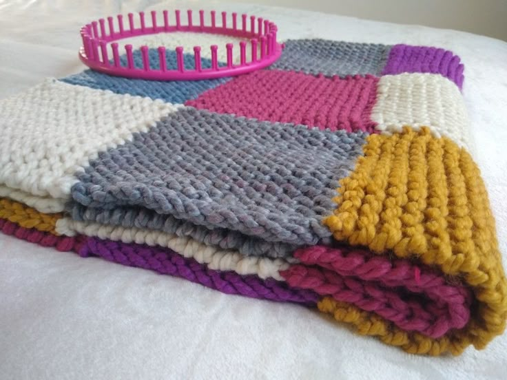 a pile of knitted blankets sitting on top of a bed next to a pink basket