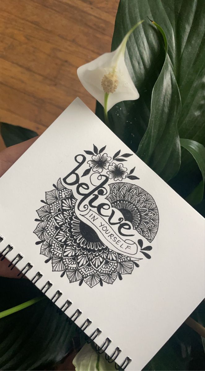 a hand holding up a notebook with the words believe on it next to some plants