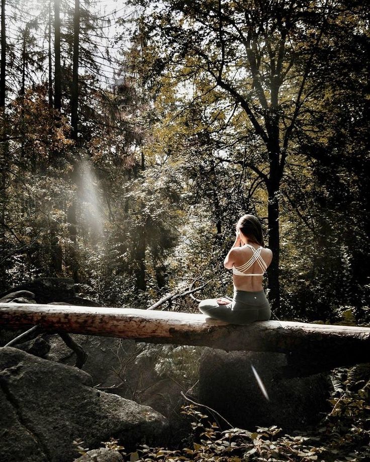 a woman is sitting on a log in the middle of a forest with trees and rocks