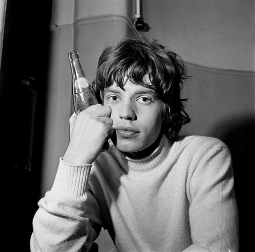 black and white photograph of a man holding a beer in front of his face while talking on the phone