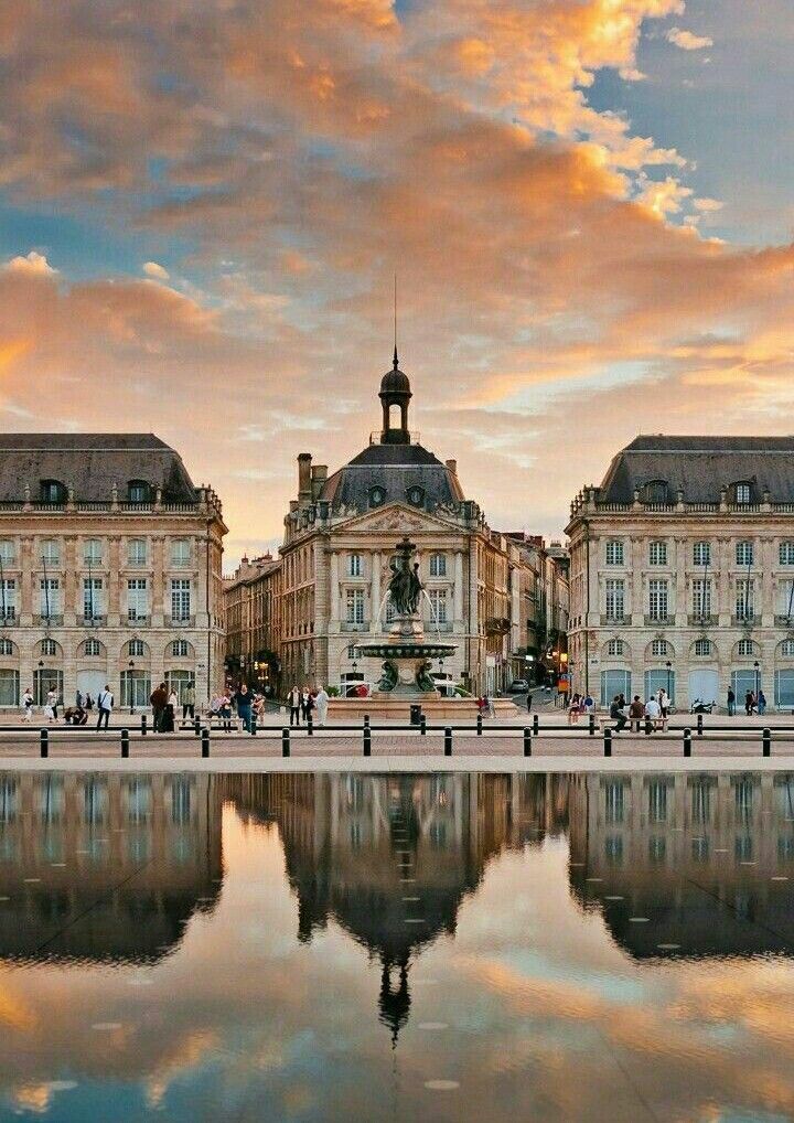 people are walking on the sidewalk in front of some buildings with water reflecting off it