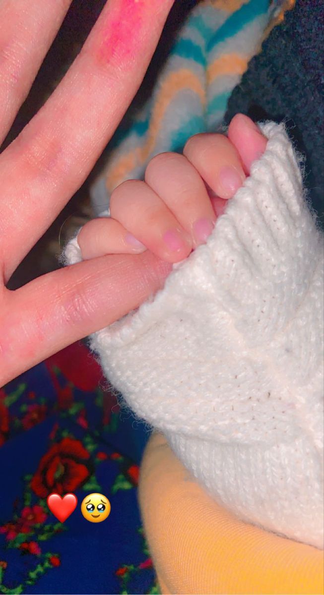 a baby's hand is holding the finger of someone with pink nail polish on it