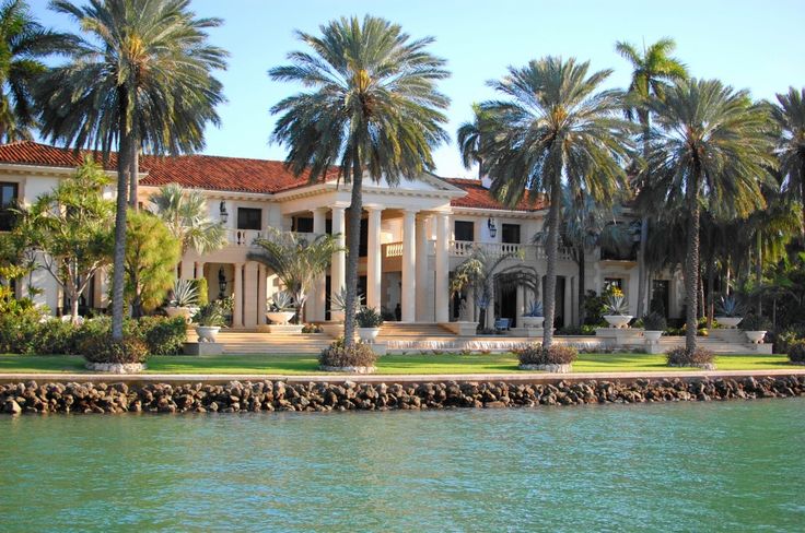 a large white house with palm trees in front of it and water behind the house