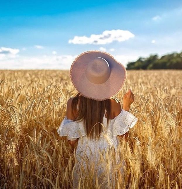 a girl in a white dress and hat standing in a wheat field with her hands up