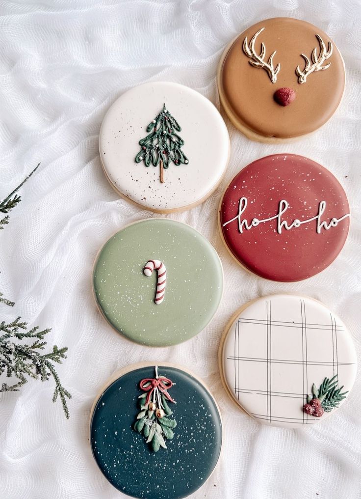 four decorated cookies sitting on top of a white sheet covered table next to a christmas tree