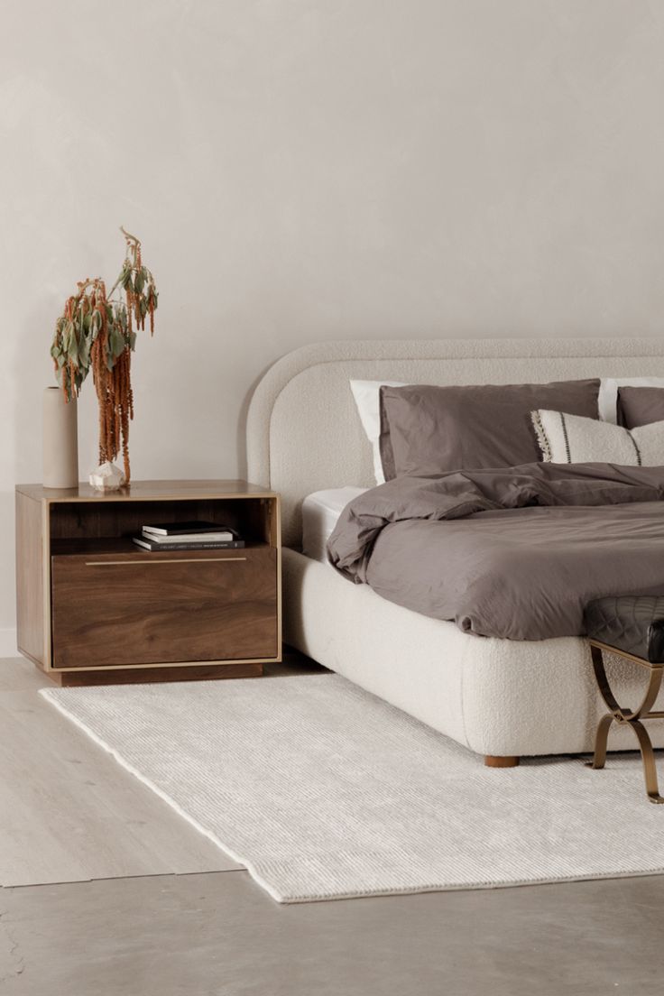 a bedroom with a bed, night stand and side table on the carpeted floor