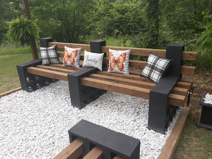 a wooden bench sitting on top of a gravel covered field next to trees and bushes