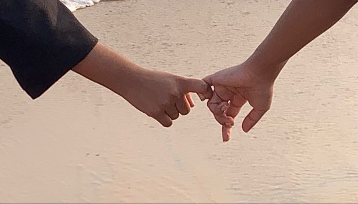 two people holding hands while walking on the beach