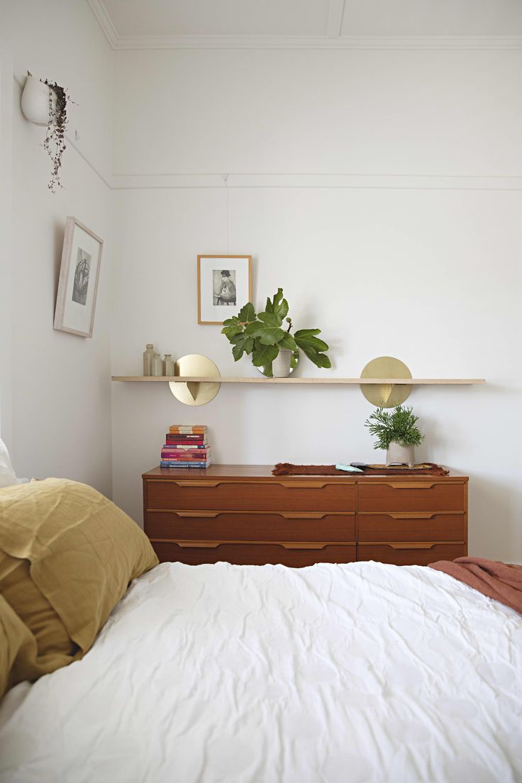 a bedroom with a bed, dresser and plants on the shelf above it's headboard