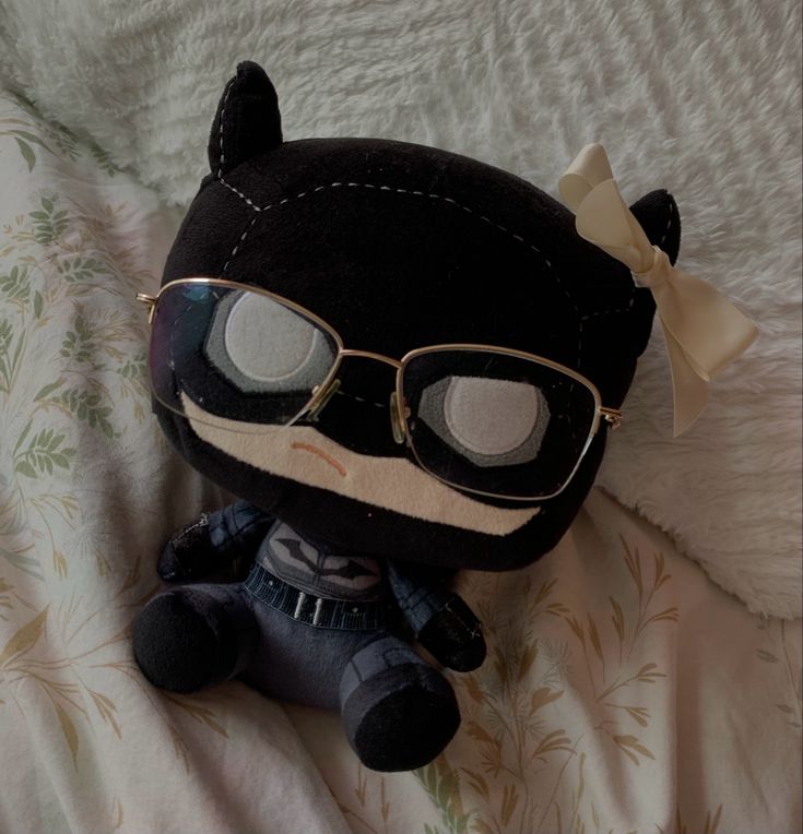 a stuffed animal with glasses and a bow on it's head sitting on a bed