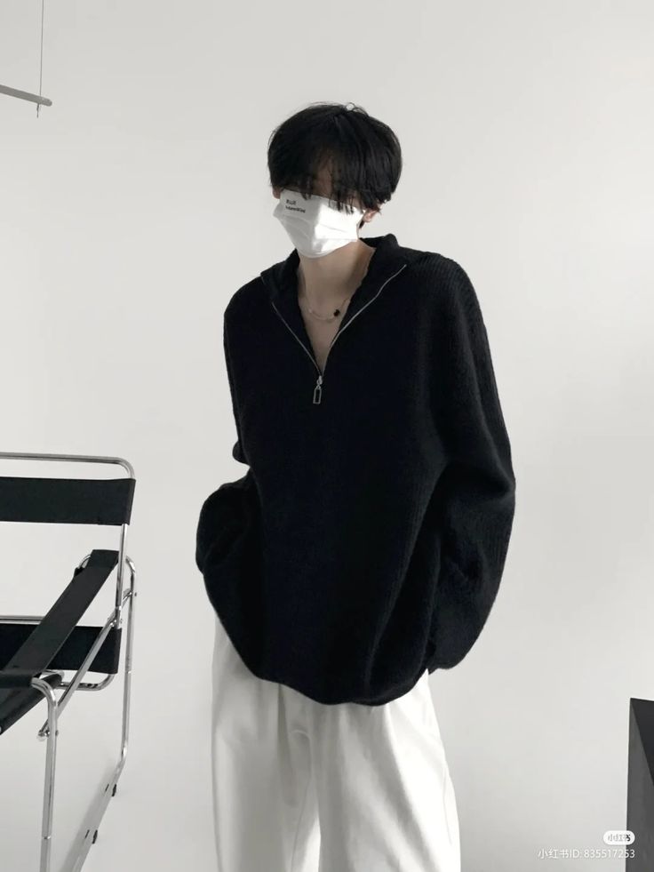 a person standing in front of a chair wearing a black sweater and white pants with a mask on his face