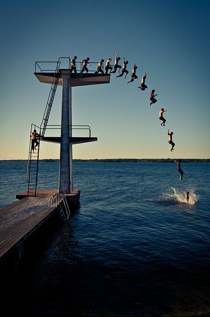 a group of people jumping into the water from a dock on a body of water