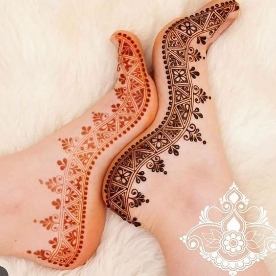 two feet with henna tattoos on them laying on a white furnishing area