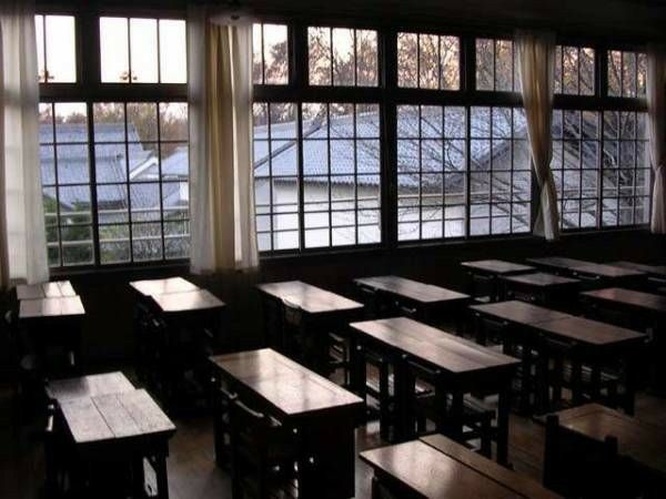 an empty classroom filled with wooden desks next to large windows and lots of windows