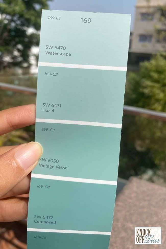 a hand holding up a pantone color swatch in front of some trees and buildings