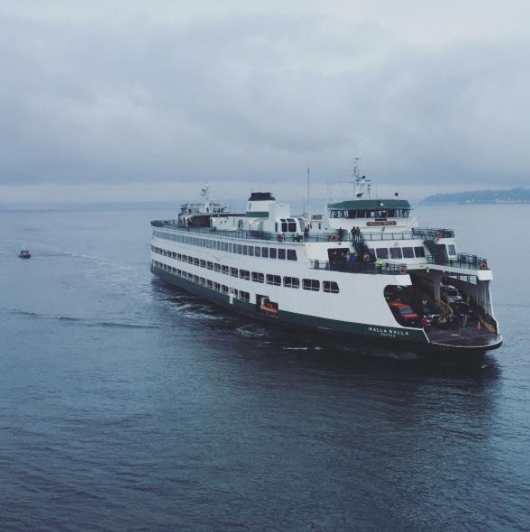 a large ferry boat in the middle of the ocean on a cloudy day with two smaller boats behind it